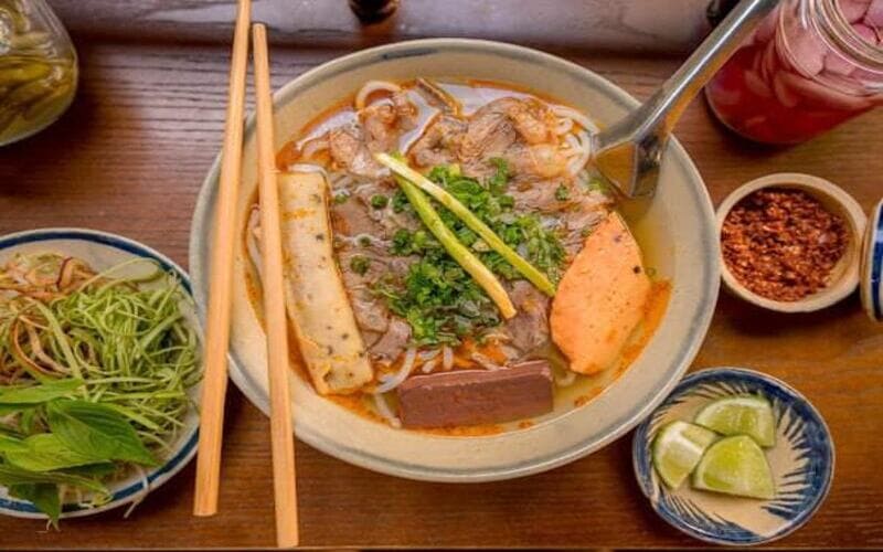 Tô bún bò kiểu miền Bắc với nước dùng đậm màu, cùng thịt bò, chả và các rau sống ăn kèm